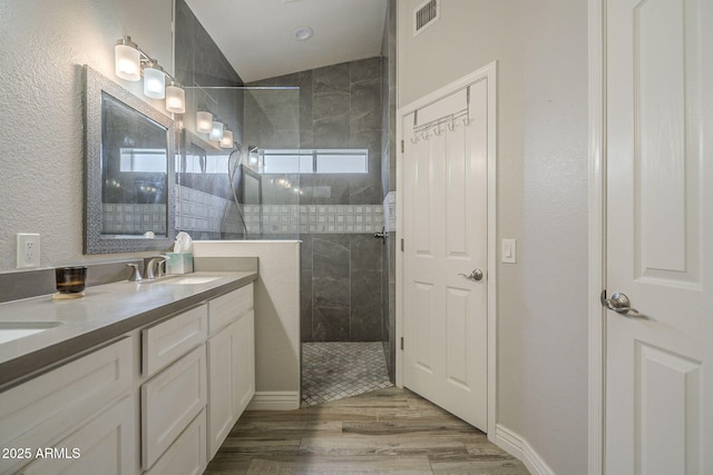 full bath featuring walk in shower, double vanity, wood finished floors, and vaulted ceiling