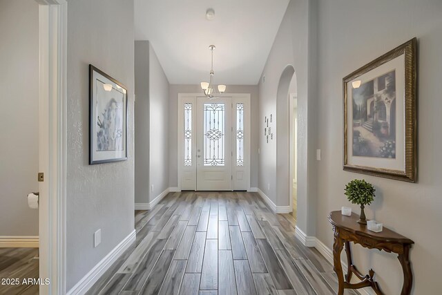 foyer entrance featuring wood finished floors, baseboards, lofted ceiling, a chandelier, and arched walkways