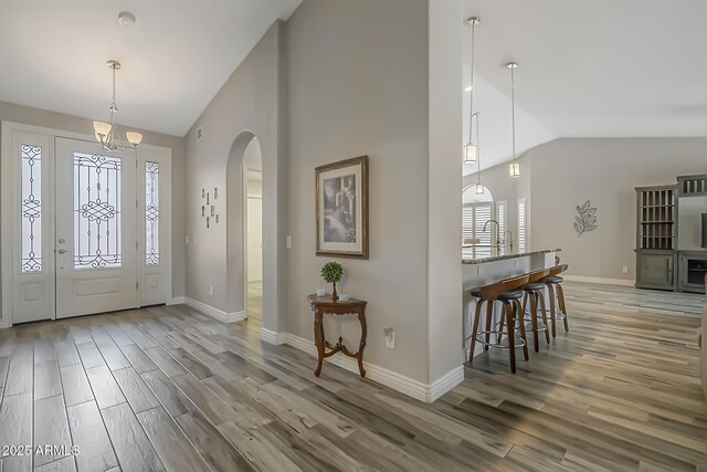 entryway featuring wood finished floors, arched walkways, baseboards, a chandelier, and high vaulted ceiling