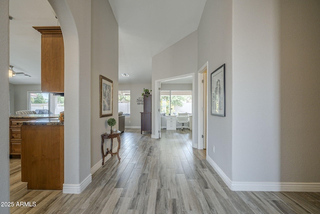 hallway with arched walkways, light wood-style floors, and baseboards