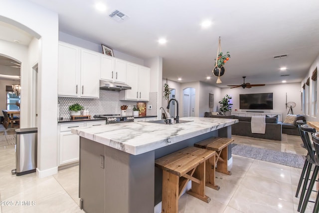 kitchen featuring visible vents, arched walkways, decorative backsplash, gas range, and under cabinet range hood