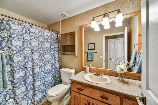 bathroom featuring toilet, vanity, a textured wall, and visible vents