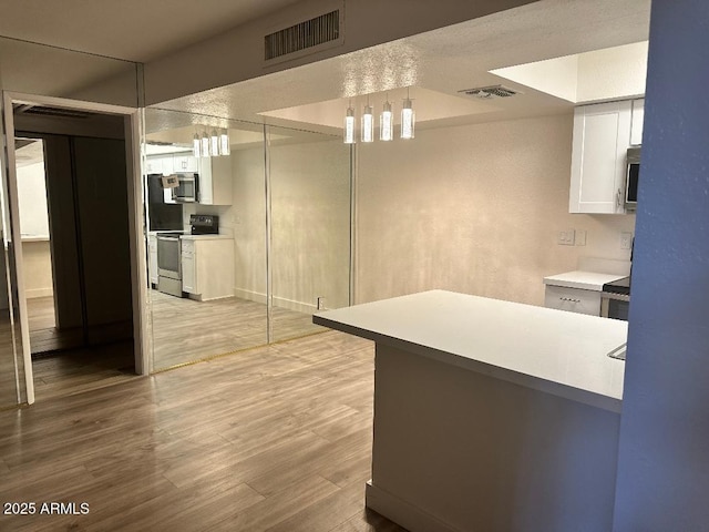 kitchen with pendant lighting, stainless steel appliances, white cabinetry, and light hardwood / wood-style flooring