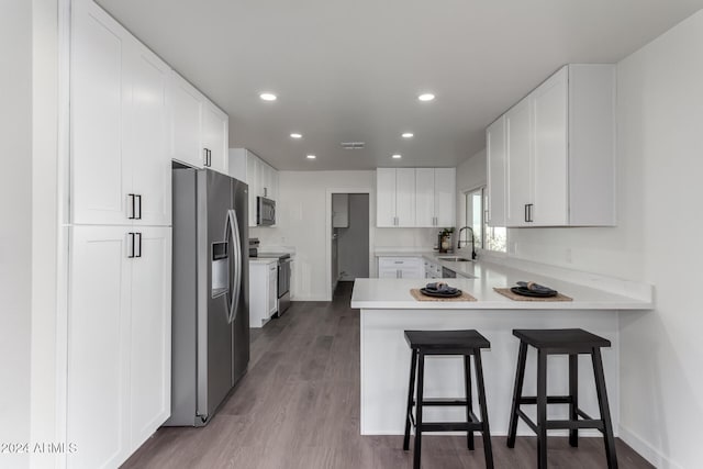 kitchen with kitchen peninsula, appliances with stainless steel finishes, a kitchen breakfast bar, sink, and white cabinets