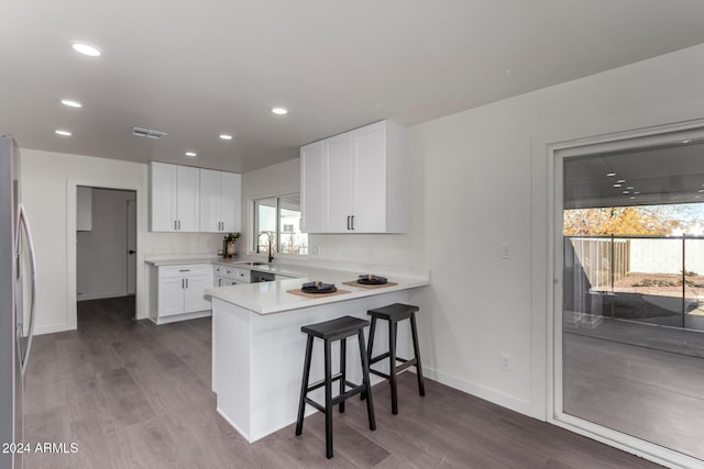 kitchen with kitchen peninsula, a breakfast bar, sink, stainless steel fridge with ice dispenser, and white cabinetry