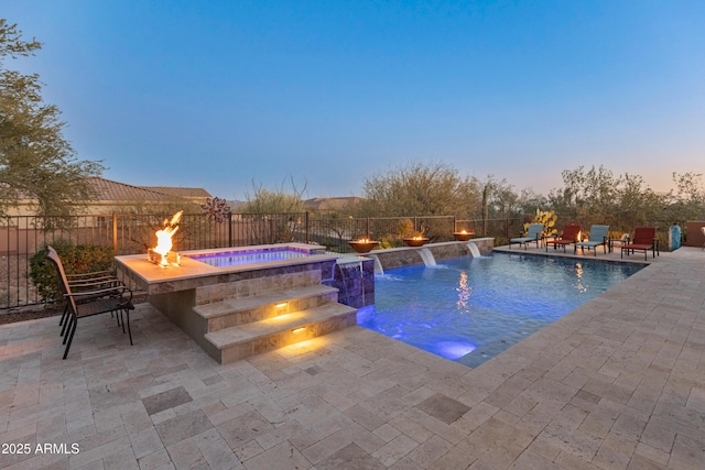 pool at dusk featuring an in ground hot tub, pool water feature, a patio, and a fire pit