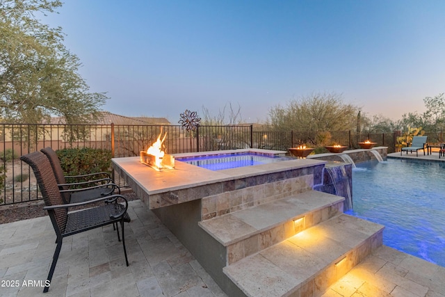 pool at dusk featuring a fire pit, a patio area, and pool water feature