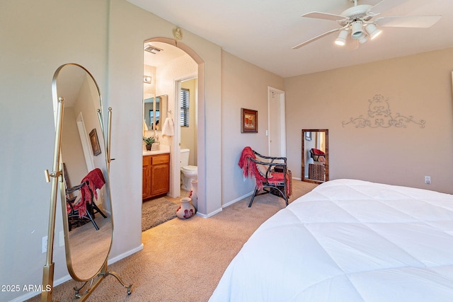 bedroom featuring light carpet, ensuite bathroom, and ceiling fan