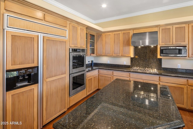 kitchen with wall chimney range hood, stainless steel appliances, ornamental molding, decorative backsplash, and dark stone counters