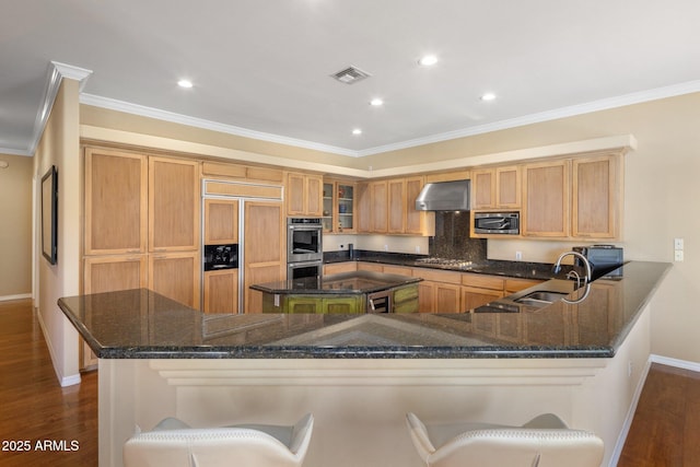 kitchen featuring built in appliances, wall chimney exhaust hood, a kitchen bar, and kitchen peninsula