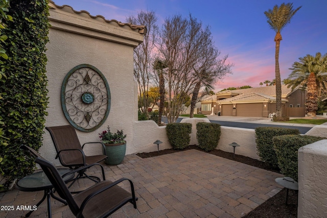 patio terrace at dusk featuring a garage