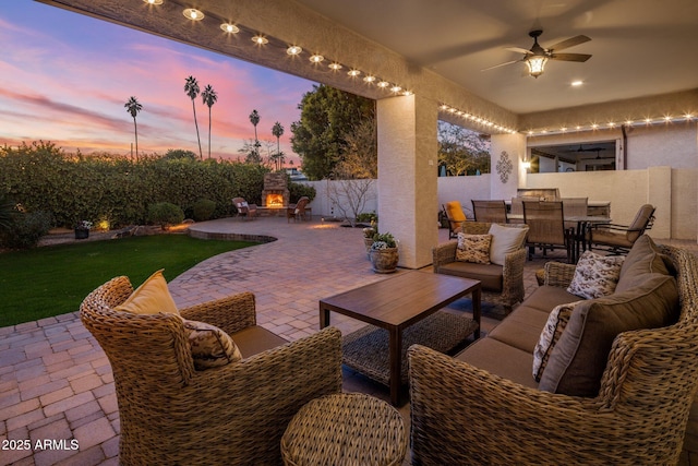 patio terrace at dusk with ceiling fan and an outdoor living space with a fireplace