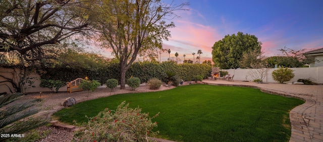 yard at dusk with exterior fireplace and a patio