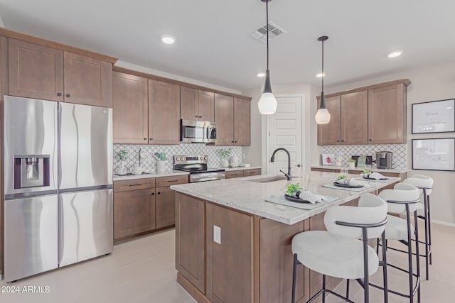 kitchen with visible vents, appliances with stainless steel finishes, a sink, light stone countertops, and a kitchen bar