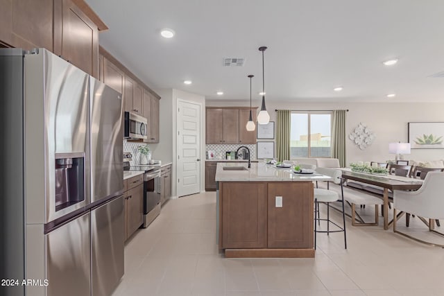 kitchen featuring a breakfast bar, a sink, appliances with stainless steel finishes, backsplash, and an island with sink