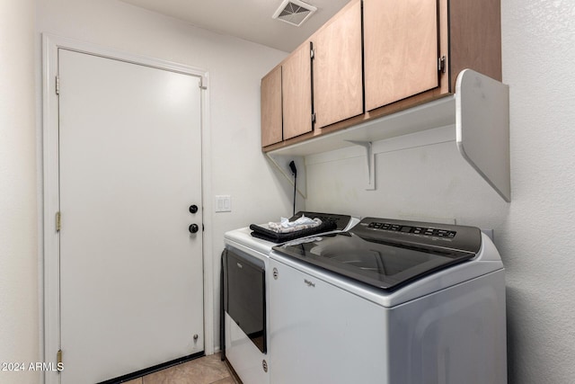 clothes washing area featuring cabinets, light tile patterned floors, and washing machine and clothes dryer