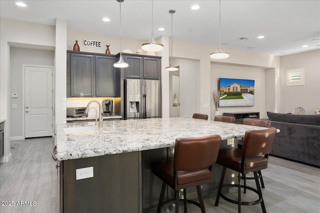 29344 N 132nd Ln, Peoria, AZ 85383 - kitchen featuring stainless steel fridge, light stone counters, open floor plan, light wood-style flooring, and a kitchen bar