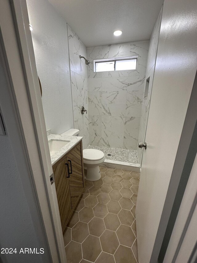 bathroom with a tile shower, a textured ceiling, tile patterned floors, toilet, and vanity