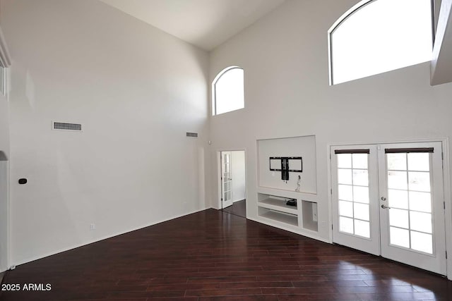 unfurnished living room with a high ceiling, french doors, and wood finished floors