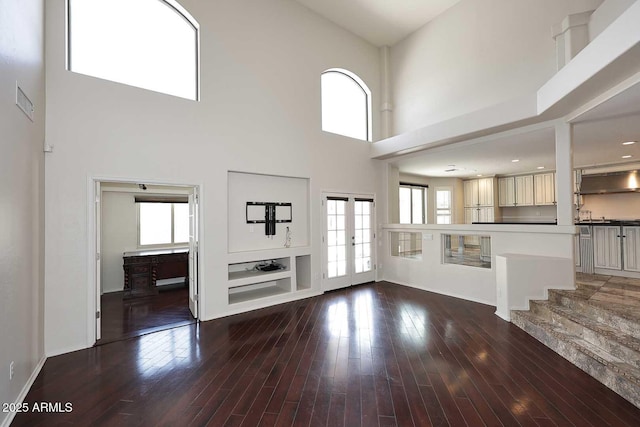 unfurnished living room featuring a towering ceiling, wood-type flooring, and french doors