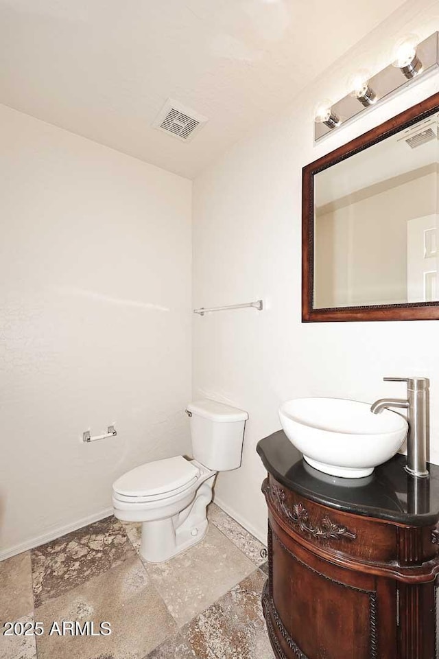 half bath with baseboards, vanity, toilet, and stone finish floors