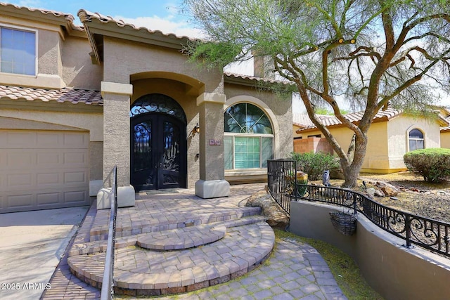 property entrance with stucco siding, a tile roof, a garage, french doors, and fence