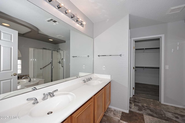 full bath featuring stone finish flooring, a shower stall, baseboards, double vanity, and a spacious closet