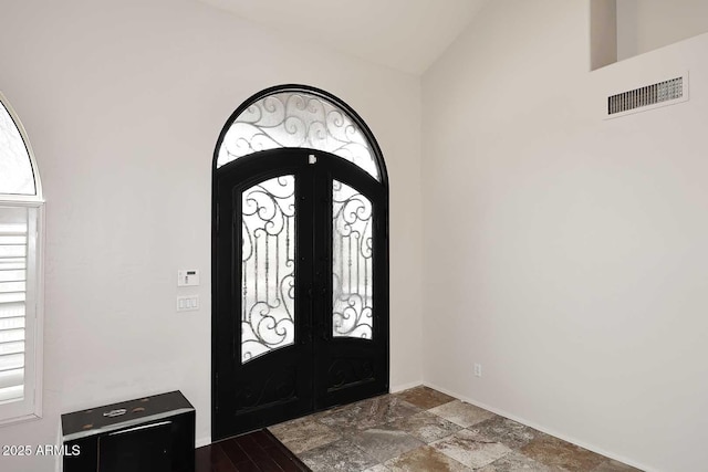 foyer featuring lofted ceiling, french doors, dark stone finish flooring, arched walkways, and baseboards