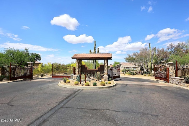 view of asphalt road with a gate, a gated entry, and curbs