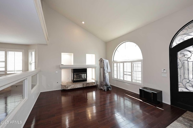 unfurnished living room featuring high vaulted ceiling, wood finished floors, a glass covered fireplace, and baseboards