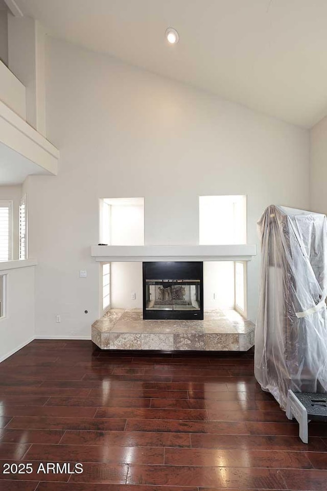 unfurnished living room featuring hardwood / wood-style floors, a glass covered fireplace, plenty of natural light, recessed lighting, and high vaulted ceiling