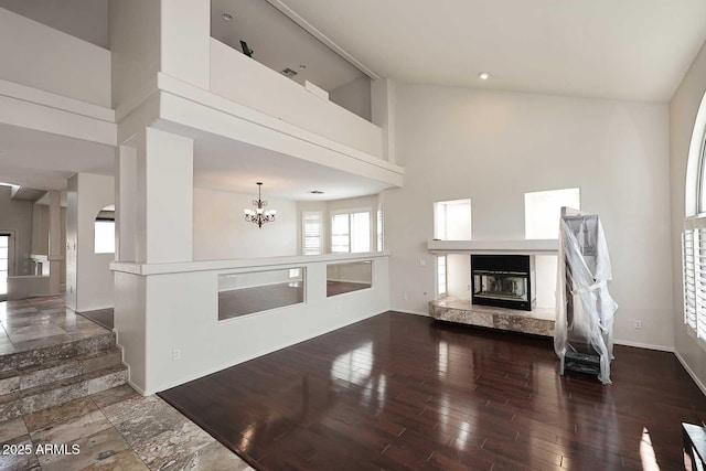 unfurnished living room featuring a glass covered fireplace, a towering ceiling, plenty of natural light, a chandelier, and baseboards