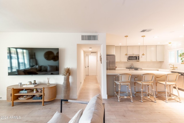 kitchen with a breakfast bar, sink, light wood-type flooring, decorative light fixtures, and stainless steel appliances