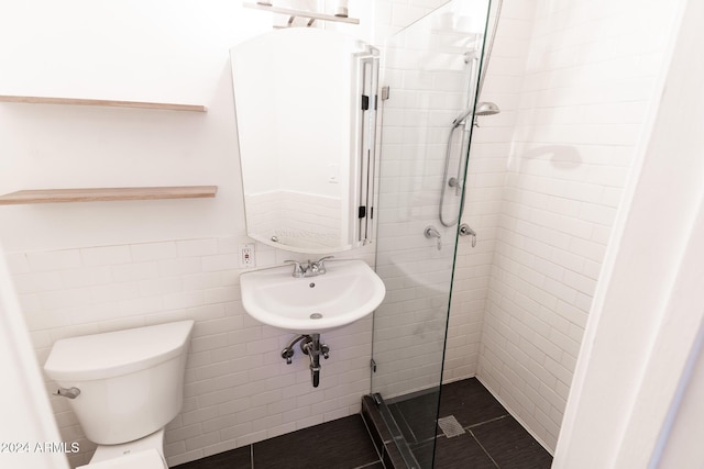 bathroom with a shower with door, tile patterned floors, sink, toilet, and tile walls