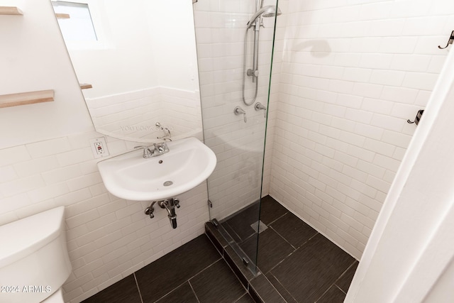 bathroom with a tile shower, sink, tile patterned floors, toilet, and tile walls