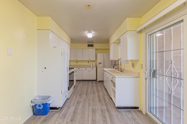 kitchen with white appliances, a sink, white cabinets, light countertops, and light wood-type flooring
