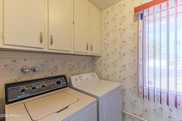 clothes washing area featuring a healthy amount of sunlight, wallpapered walls, separate washer and dryer, and cabinet space