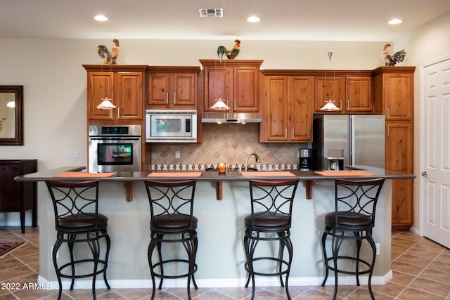 kitchen with a kitchen island with sink, brown cabinetry, visible vents, dark countertops, and appliances with stainless steel finishes