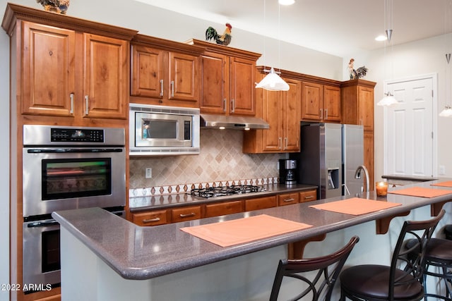 kitchen with brown cabinetry, dark countertops, tasteful backsplash, under cabinet range hood, and stainless steel appliances