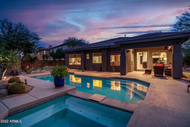 pool at dusk featuring a patio, fence, and a pool with connected hot tub