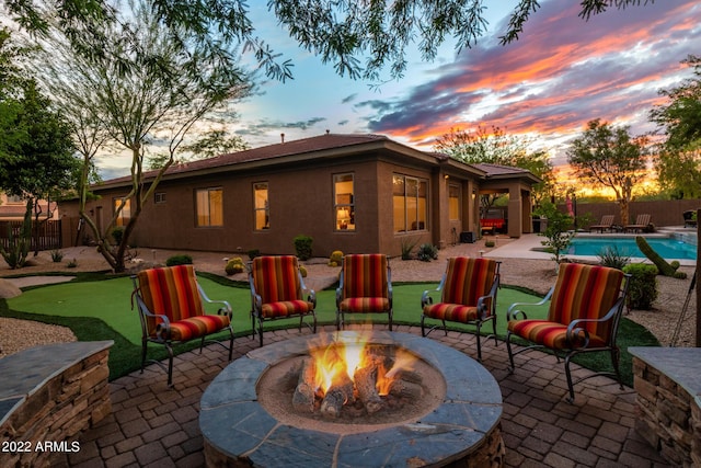 rear view of house with fence, stucco siding, a fenced in pool, a patio, and a fire pit