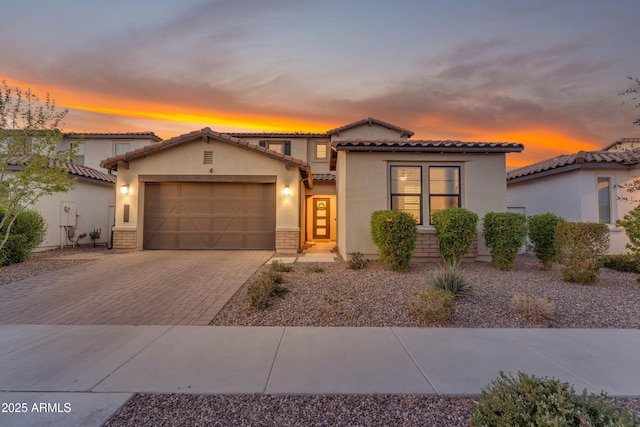 mediterranean / spanish home with a garage, decorative driveway, a tiled roof, and stucco siding