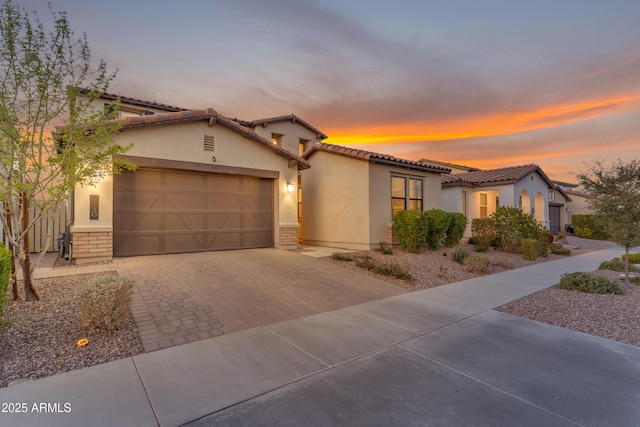 mediterranean / spanish home featuring an attached garage, a tiled roof, decorative driveway, and stucco siding