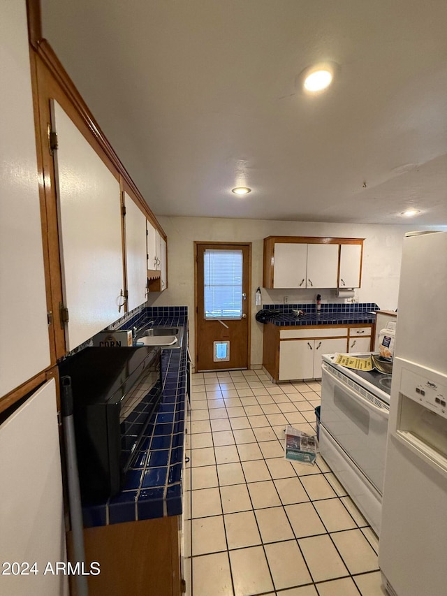 kitchen with tile counters, sink, light tile patterned floors, white cabinets, and white appliances