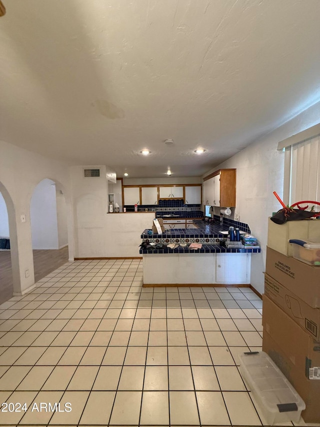 kitchen featuring tile counters, light tile patterned floors, backsplash, and kitchen peninsula