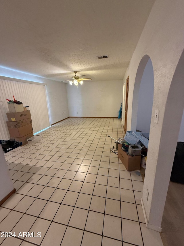 unfurnished living room with a textured ceiling, ceiling fan, and light tile patterned floors