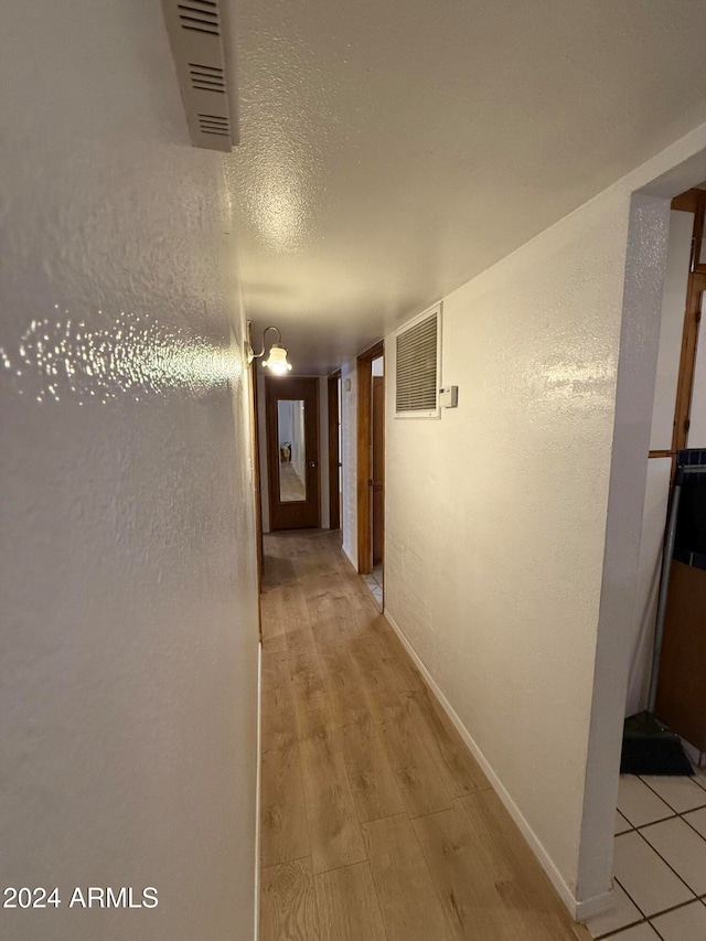 hallway with light hardwood / wood-style floors and a textured ceiling