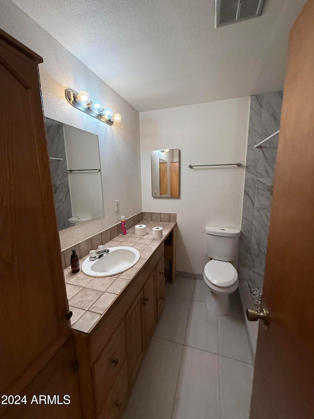 bathroom with tiled shower, toilet, tile patterned flooring, vanity, and a textured ceiling