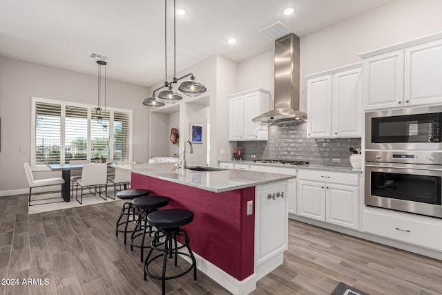 kitchen with sink, wall chimney range hood, a breakfast bar area, a kitchen island with sink, and white cabinets