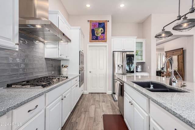 kitchen featuring white cabinetry, sink, hanging light fixtures, stainless steel appliances, and wall chimney range hood